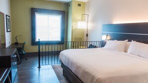 A hotel room with a large bed, a desk, a chair, a window, and a wall-mounted lamp. - Holiday Inn Express & Suites Columbia-Fort Jackson by IHG (Columbia)