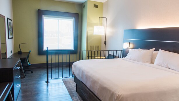 A hotel room with a large bed, a desk, a chair, a window, and a wall-mounted lamp. - Holiday Inn Express & Suites Columbia-Fort Jackson by IHG (Columbia)