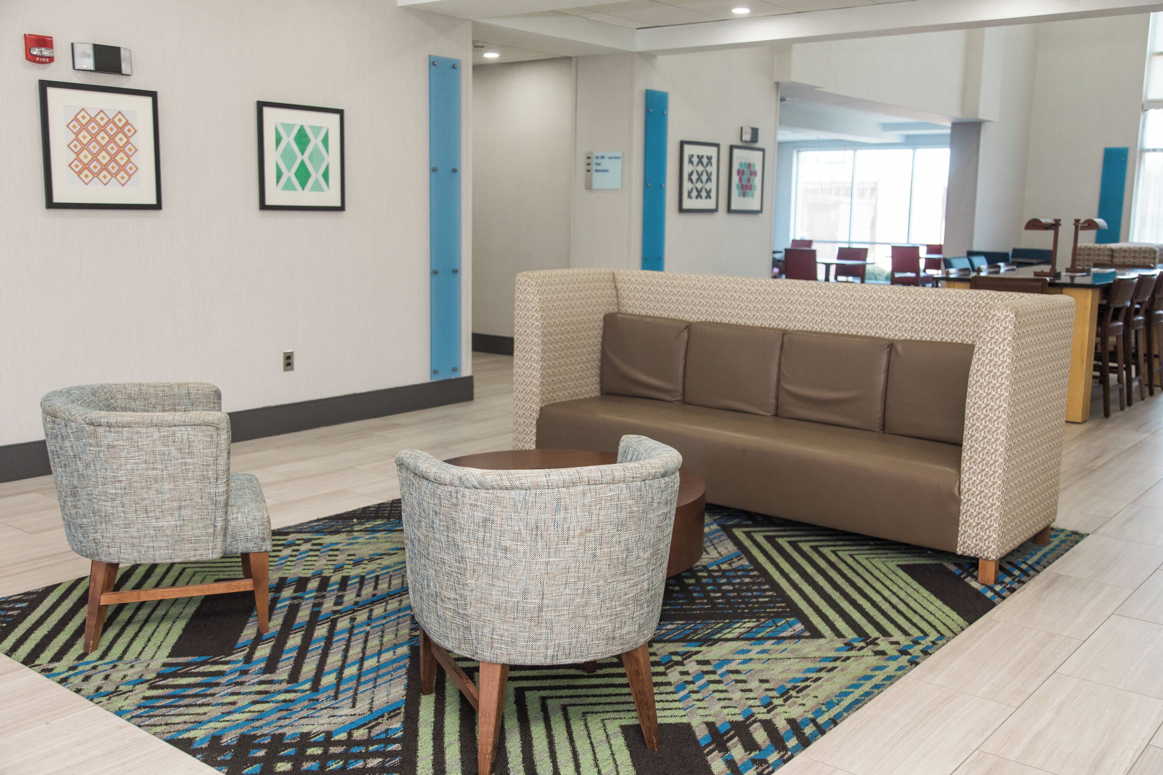 Ein moderner Lounge-Bereich mit einem braunen Sofa, zwei gemusterten Sesseln und einem Teppich mit Muster.