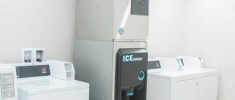 Une laverie équipée d’un grand distributeur de glaçons industriel, d’une machine à laver et d’un sèche-linge.