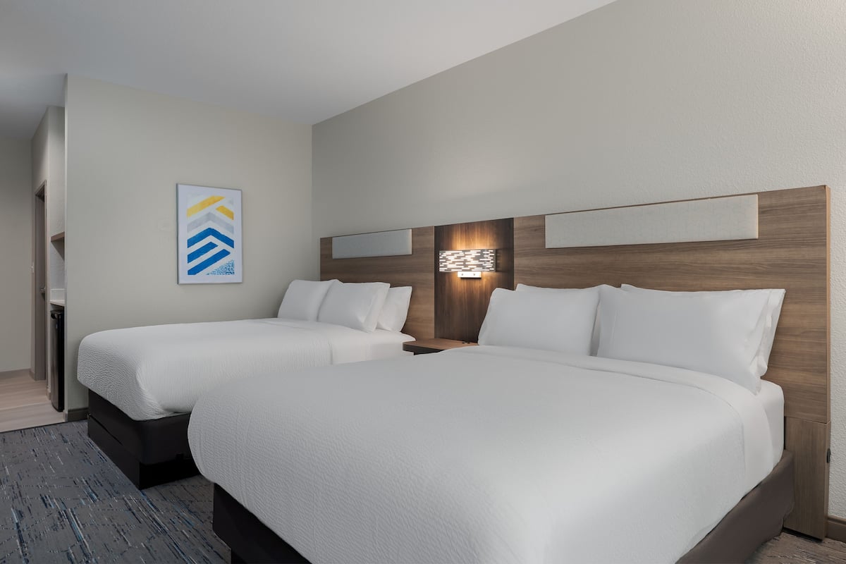 A hotel room with two beds, a nightstand, a wall-mounted light, and a piece of abstract art.