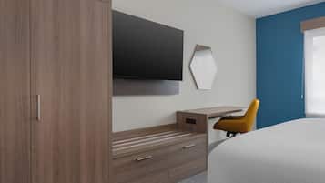 A hotel room with a bed, a wooden wardrobe, a desk with a chair, a flat-screen TV, and a mirror.