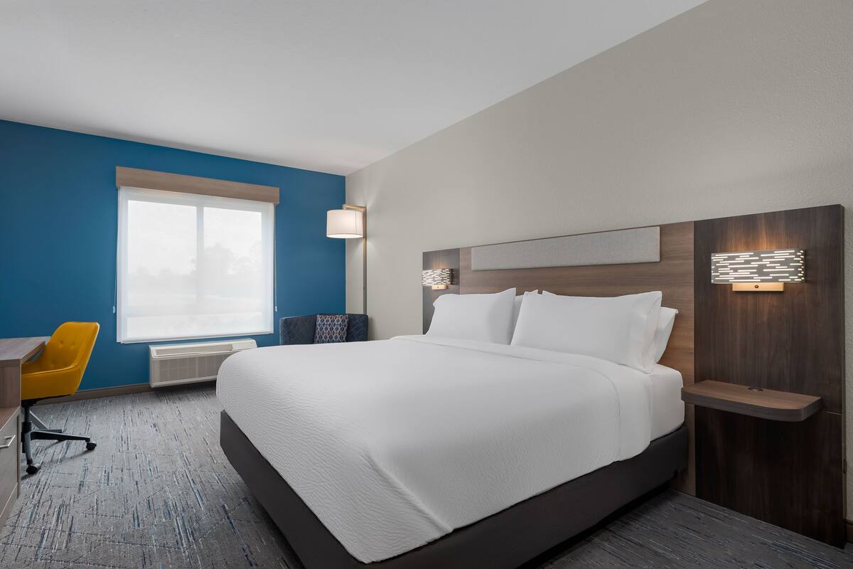 A hotel room with a large bed, a desk, a chair, and a window.