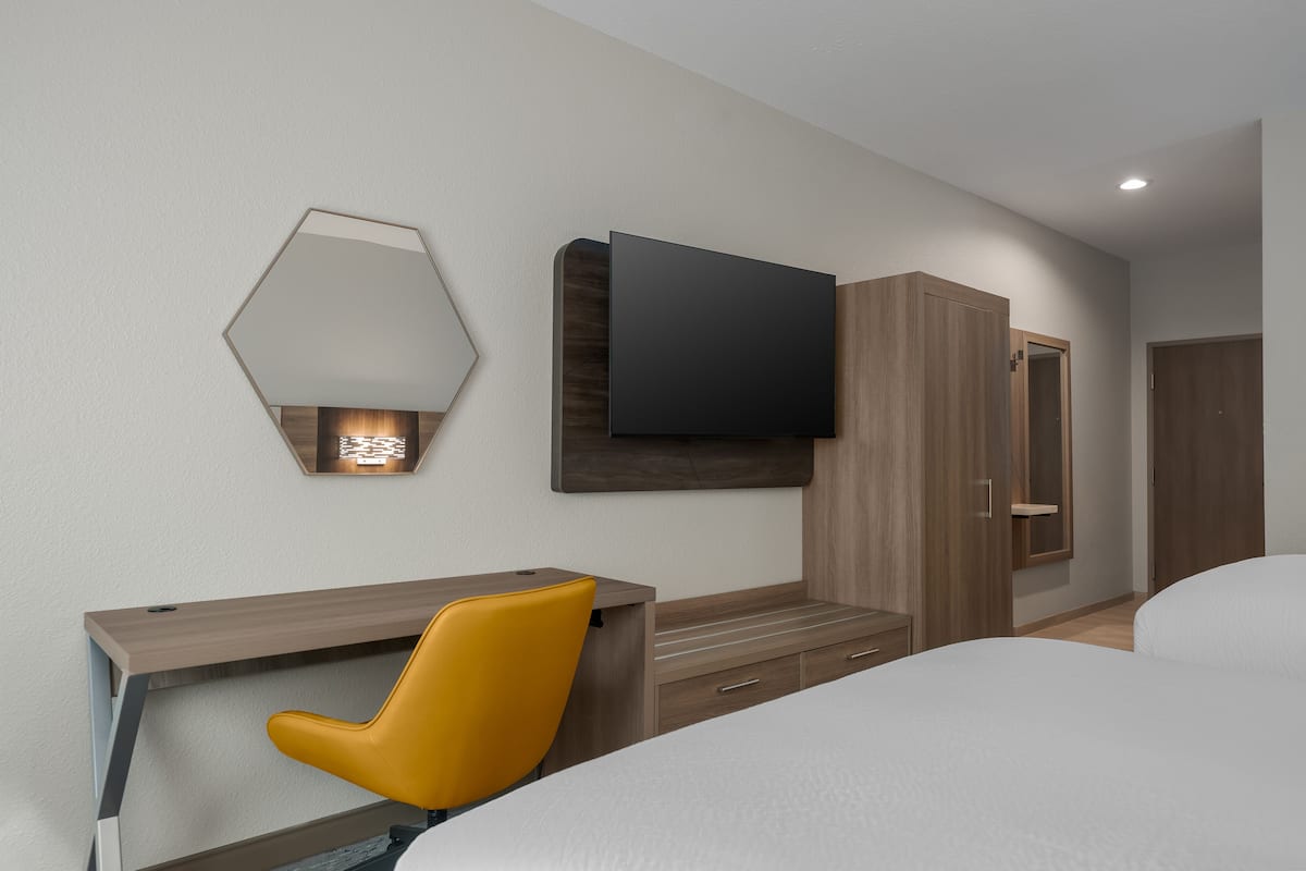 A hotel room with a bed, a desk with a chair, a TV mounted on the wall, and a wardrobe.