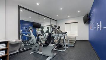 A gym with exercise equipment, a mirror, a wall-mounted TV, and a blue wall with motivational text.
