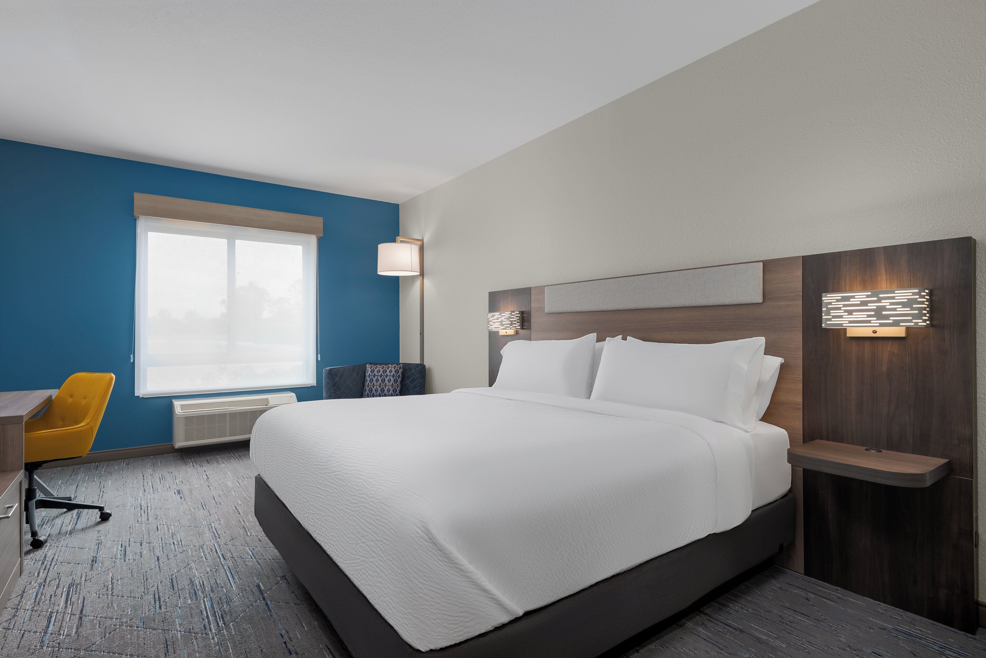 A hotel room with a large bed, a desk with a chair, and a window.