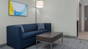 A modern room with a blue sofa, a small wooden table, a floor lamp, and a wall-mounted abstract art piece.