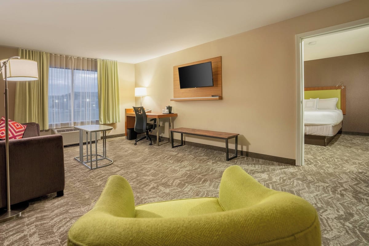 A hotel room with a bed, a desk, a chair, a lamp, a TV, and a window with curtains.