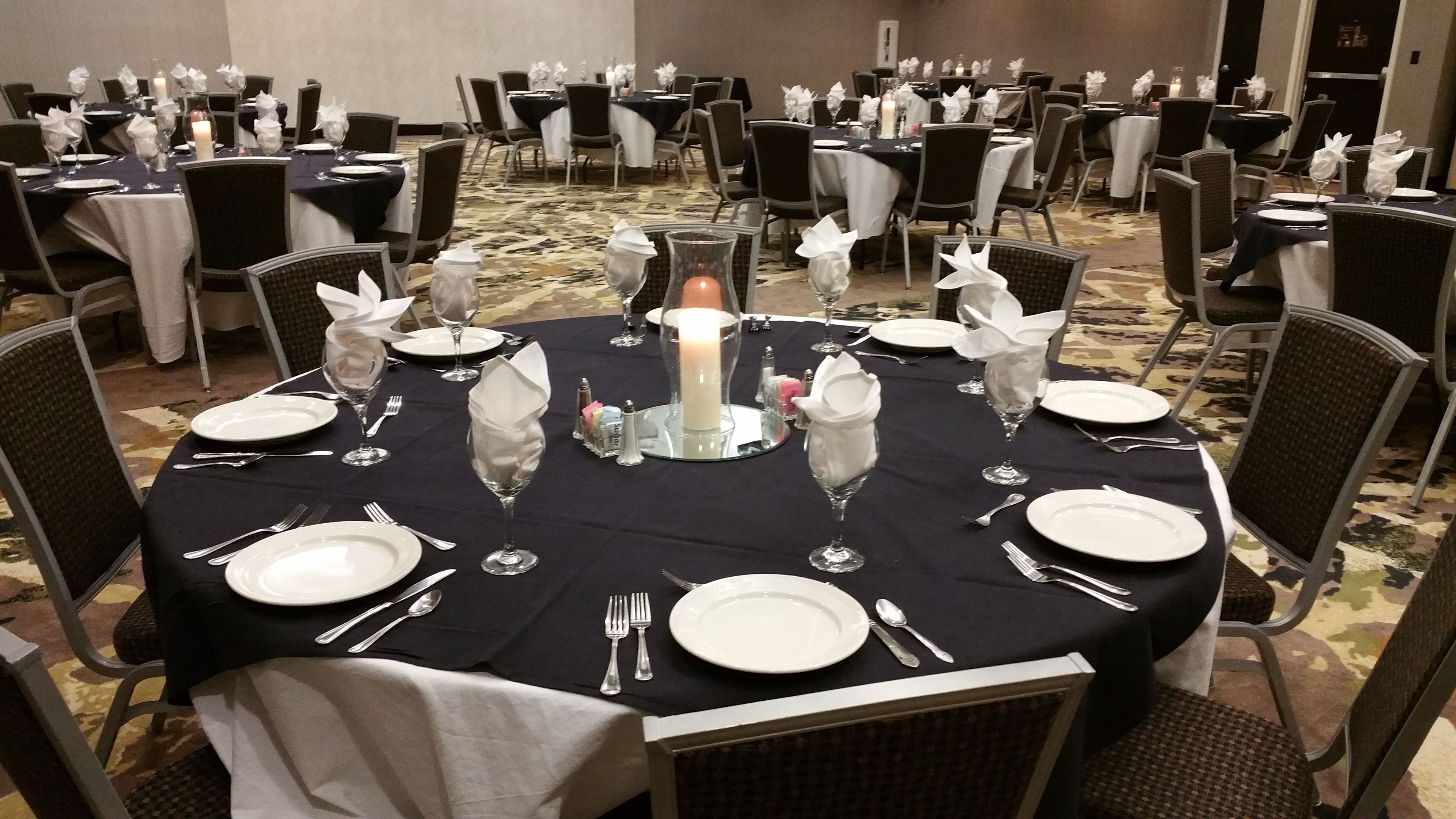 A banquet hall with round tables set for dining, each with white plates, silverware, and glassware.