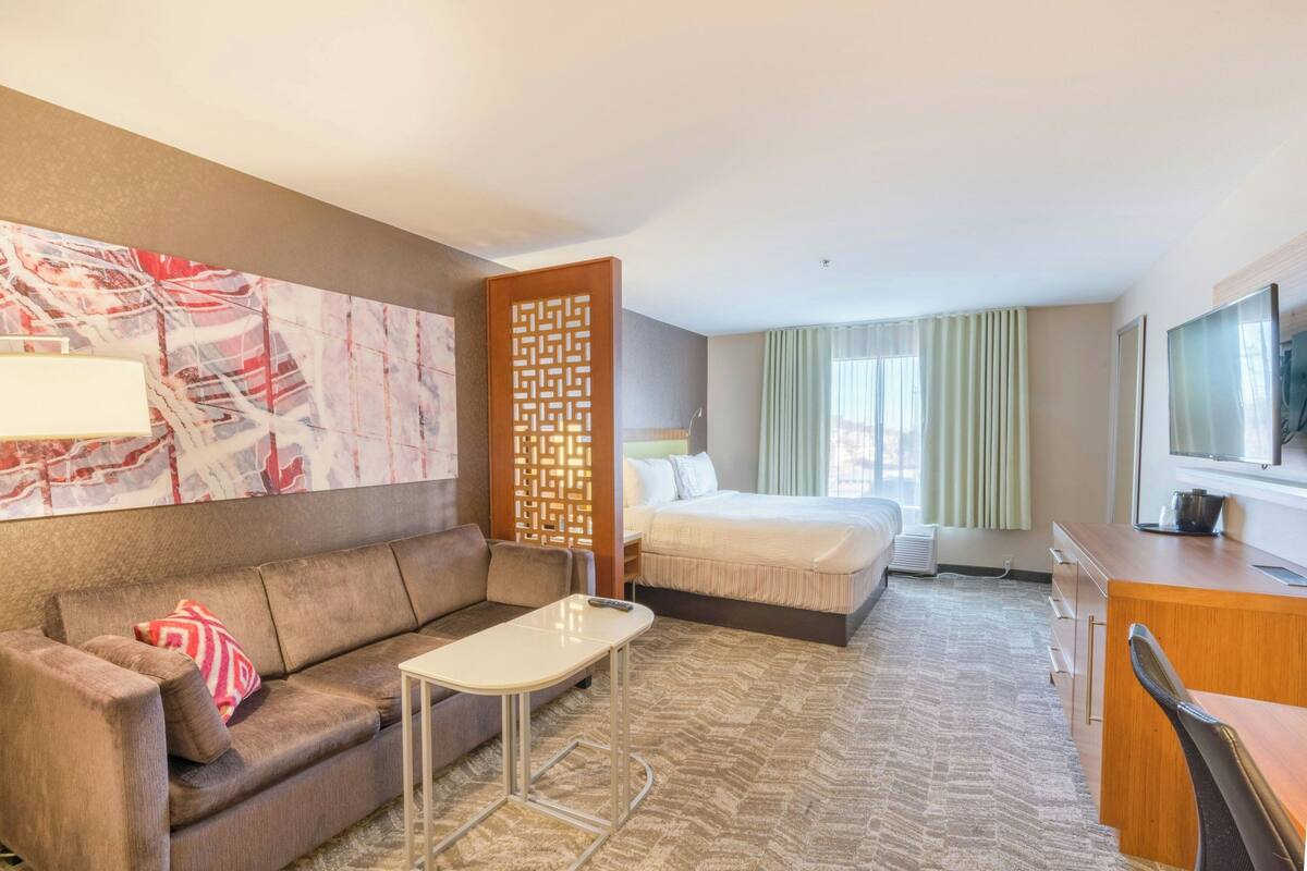A hotel room with a bed, a sofa, a desk, a television, and a decorative wall piece.