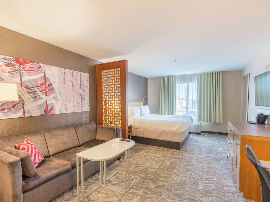 A hotel room with a bed, a sofa, a desk, a television, and a decorative wall piece.