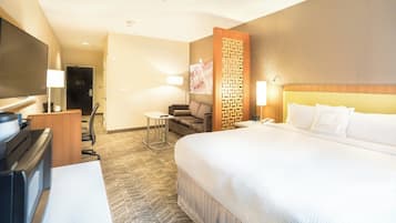 Habitación de hotel con una cama grande, un escritorio con ordenador, una silla, un televisor y un panel decorativo en la pared.