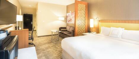 A hotel room with a large bed, a desk with a computer, a chair, a TV, and a decorative wall panel.