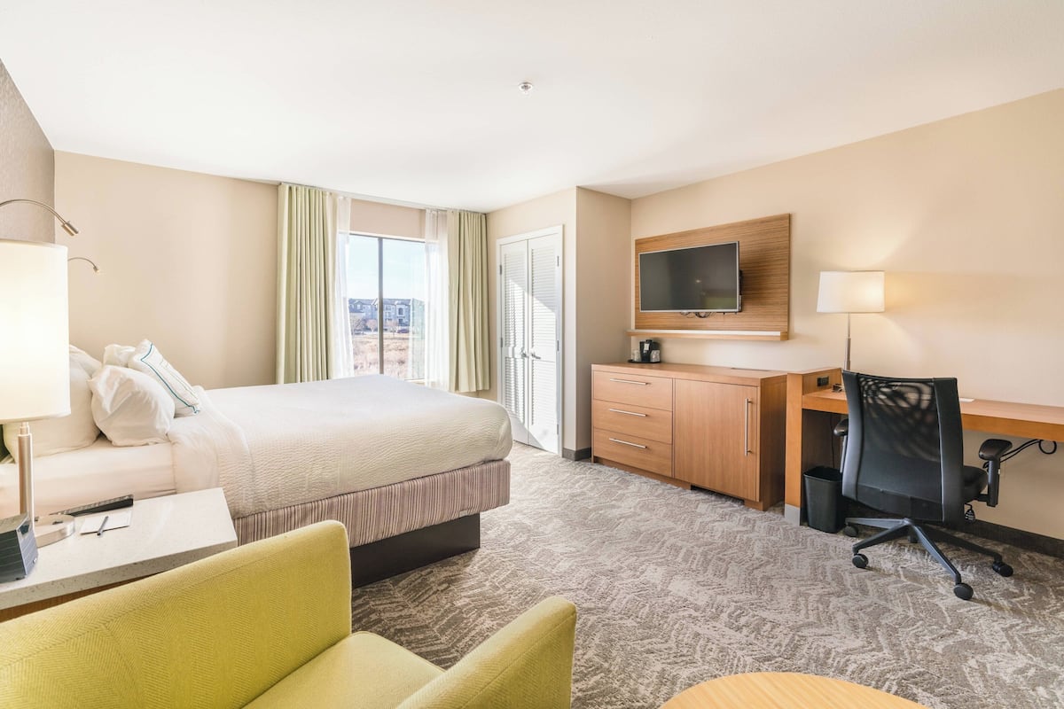 A hotel room with a bed, a desk, a chair, a TV, and a window with curtains.