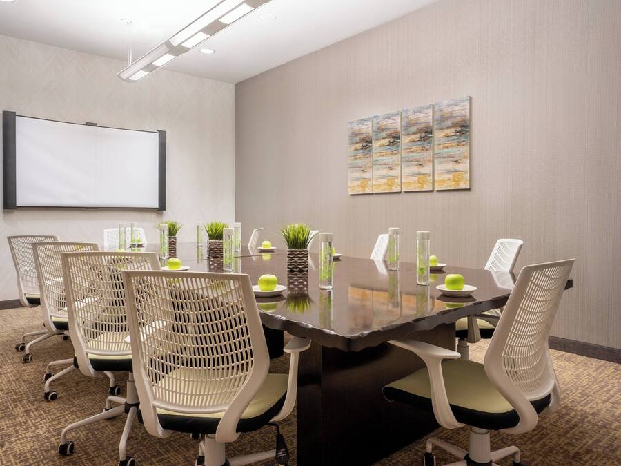 A conference room with a large table, four chairs, a whiteboard, and three paintings on the wall.