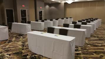 A conference room with rows of tables and chairs, carpeted floor, and exit signs on the walls.