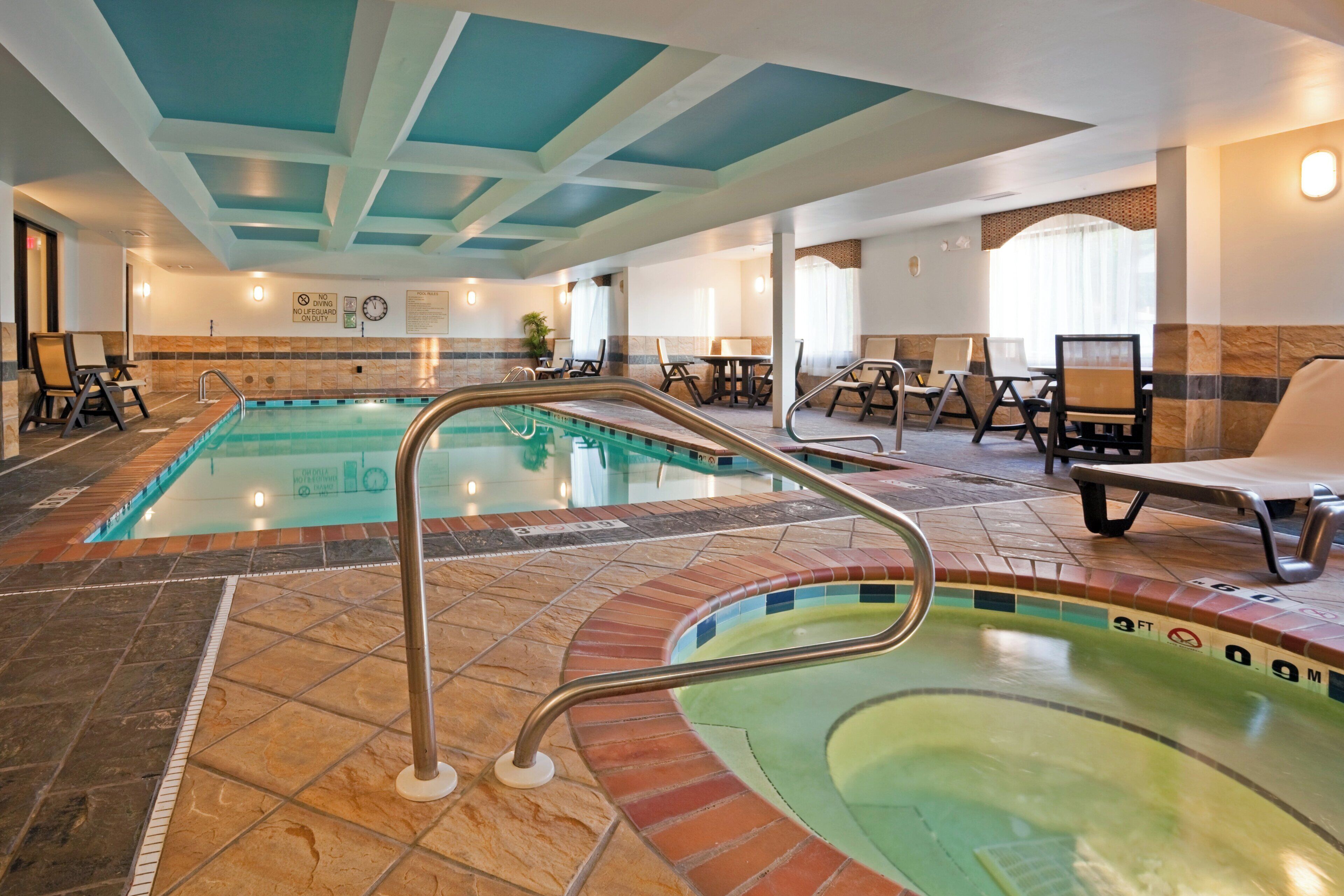 A hotel pool area with two pools, lounge chairs, and a seating area.