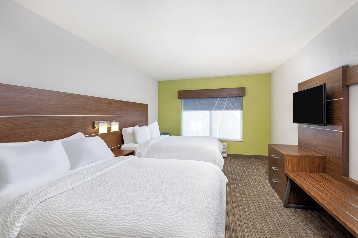 Une chambre d’hôtel avec deux lits, une télévision, un bureau et une fenêtre avec des rideaux.