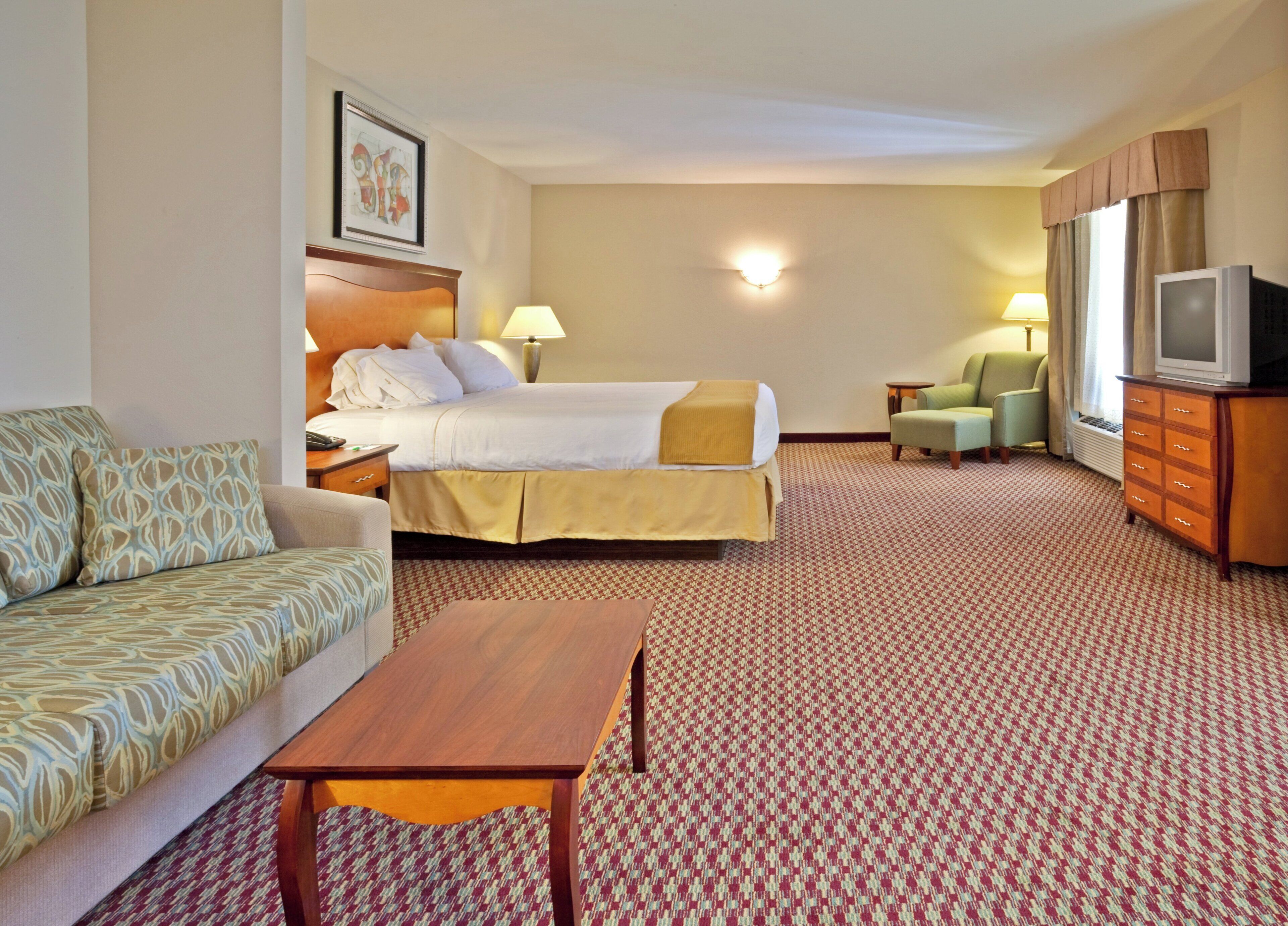 A hotel room with a bed, a sofa, a TV, a lamp, and a dresser.