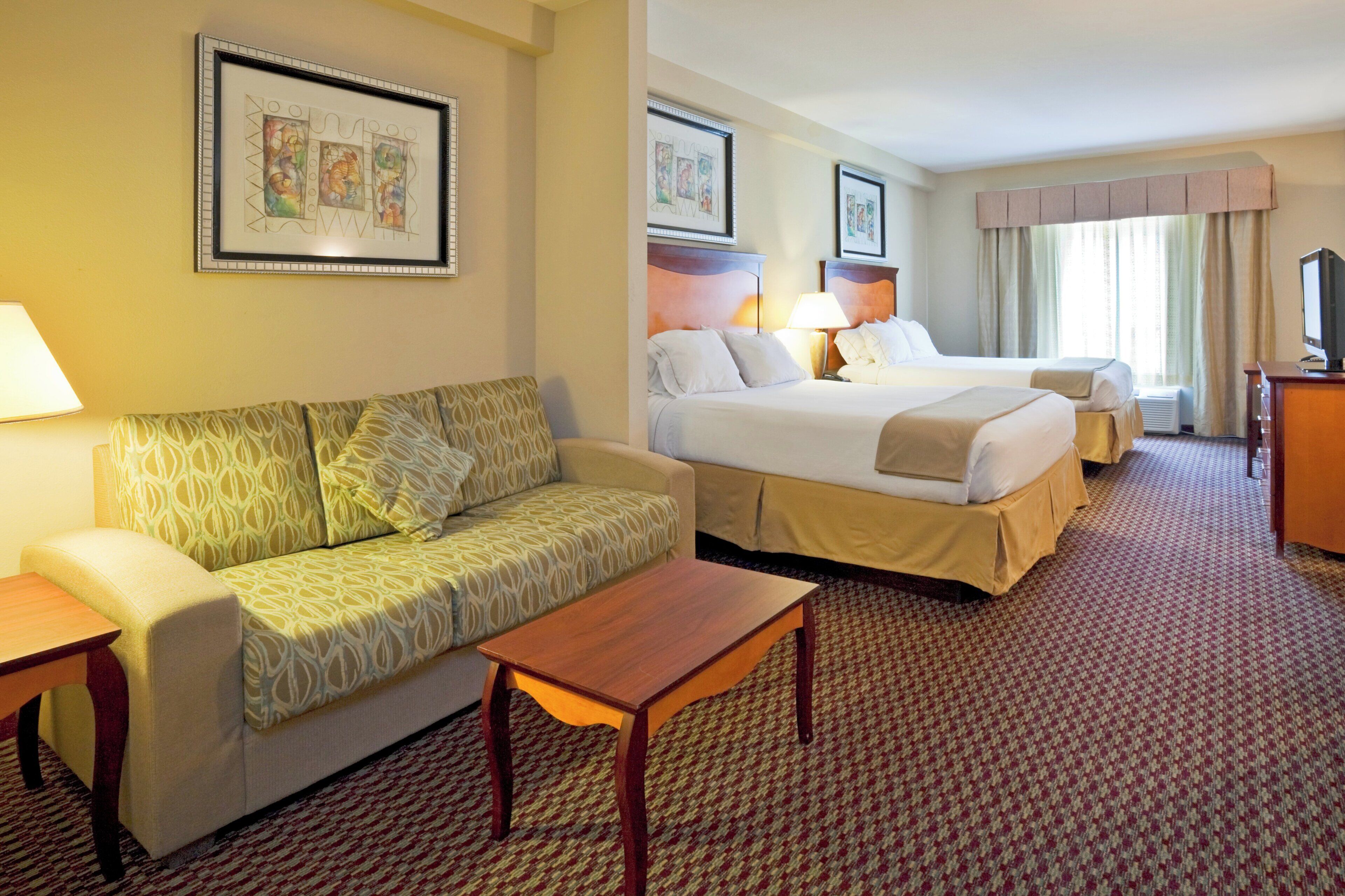 Quarto de hotel com sofá, duas camas, televisão e obras de arte nas paredes.