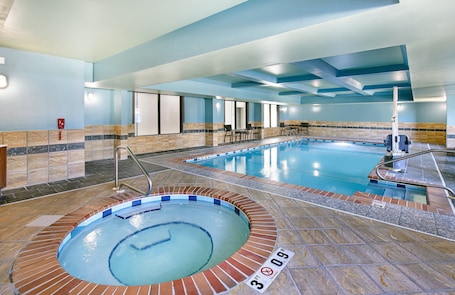 An indoor swimming pool with a hot tub, tiled flooring, and a seating area with chairs and tables.