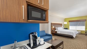 A hotel room with a kitchenette, a bed, a blue sofa, and a desk with a coffee maker.