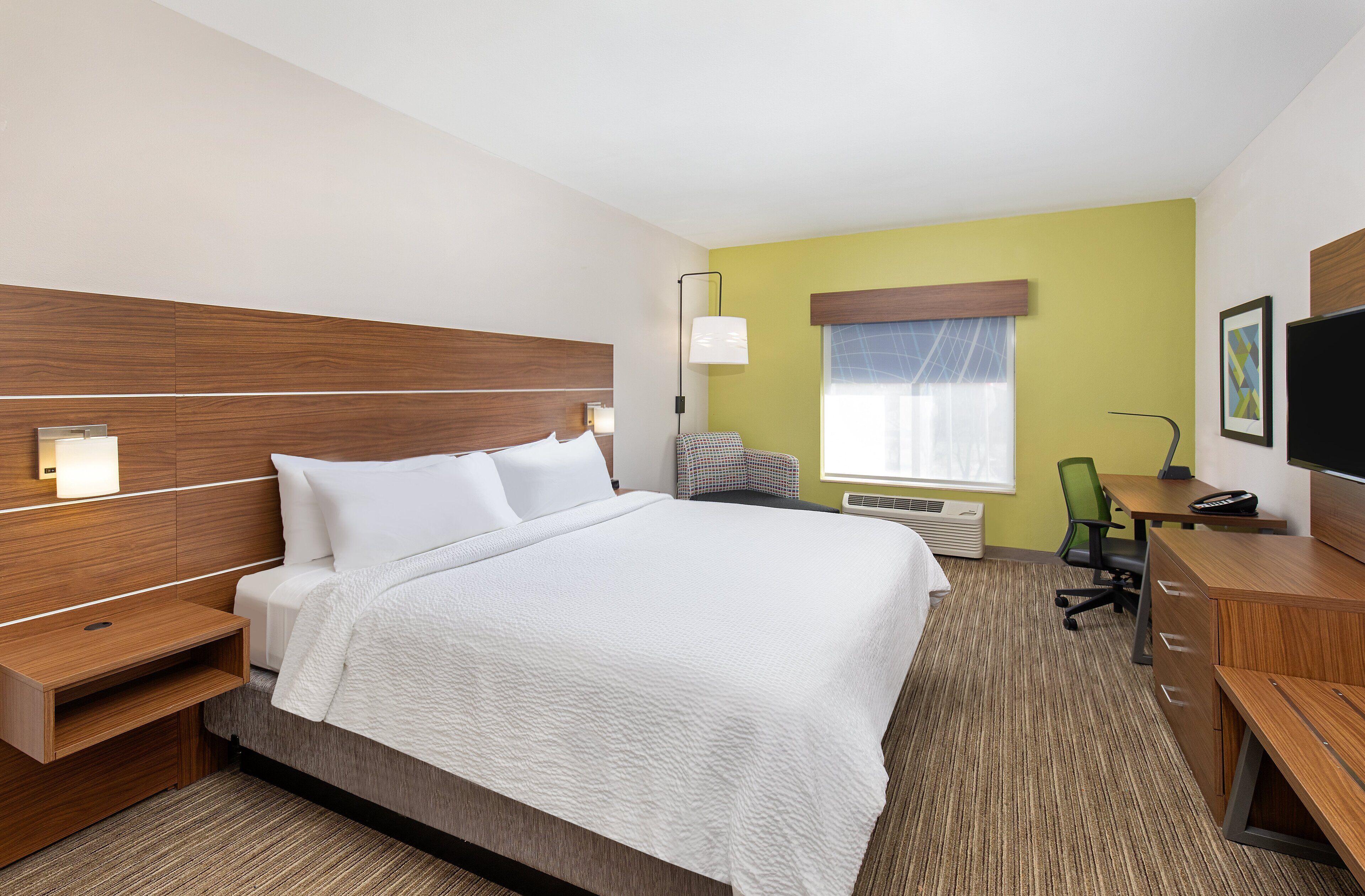 A hotel room with a bed, bedside tables, a desk, a chair, a television, and a window with blinds.