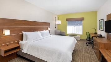 A hotel room with a bed, bedside tables, a desk, a chair, a television, and a window with blinds.
