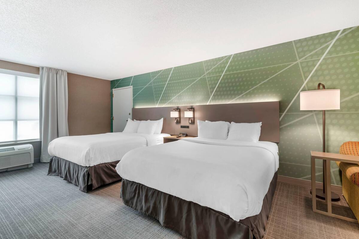 A hotel room with two beds, a desk, a chair, a lamp, and a window with curtains.