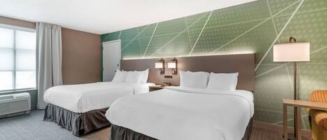 Habitación de hotel con dos camas, un escritorio, una silla, una lámpara y una ventana con cortinas.