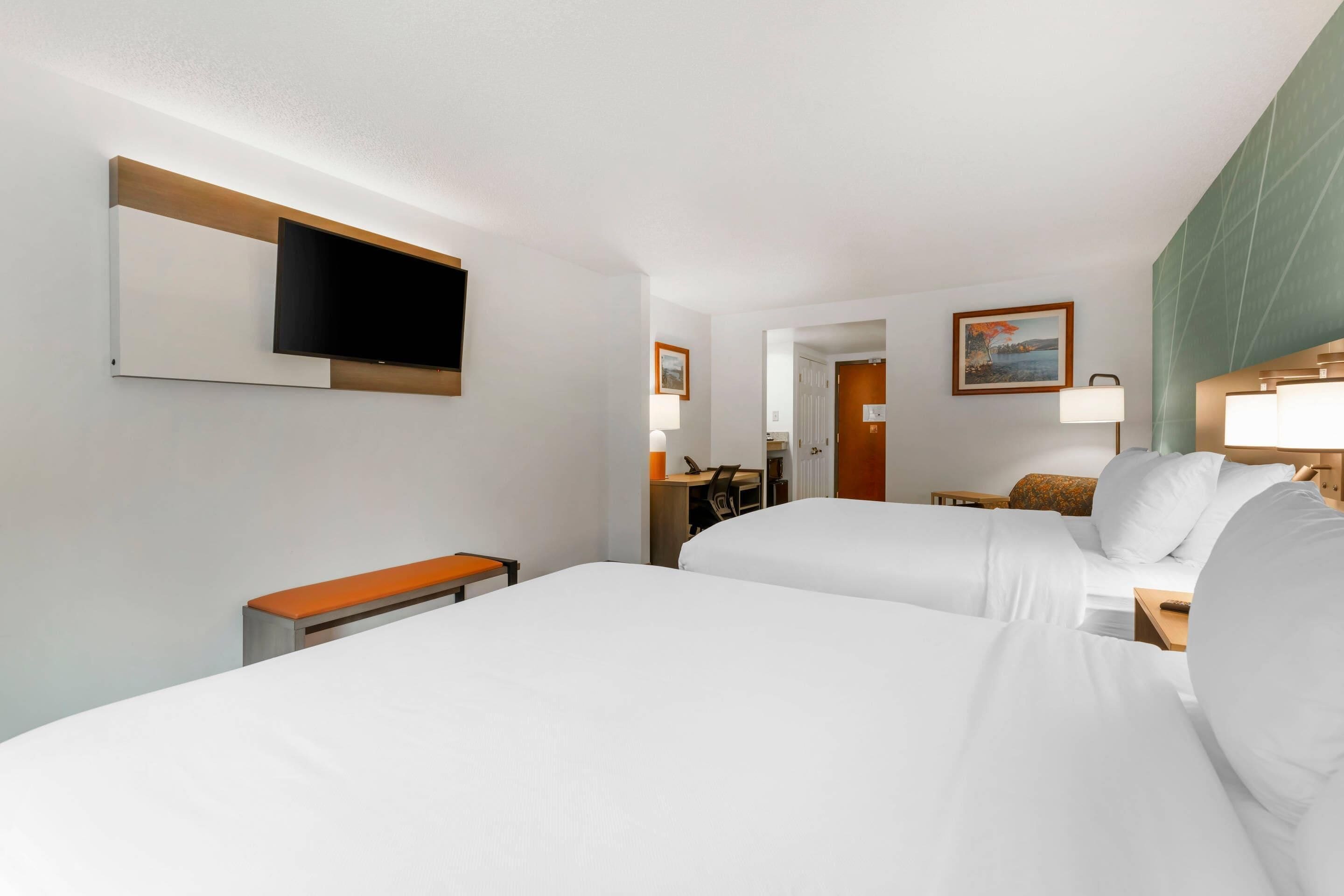 A hotel room with two beds, a desk, a chair, a television, and a painting on the wall.