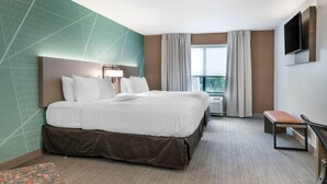 A hotel room with a large bed, a bench, a TV, and a window with curtains. - Comfort Inn & Suites Lake George (Lake George)