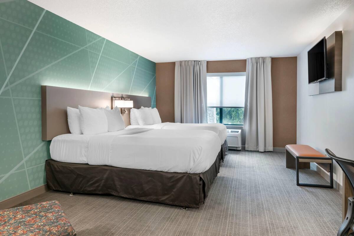A hotel room with a large bed, a bench, a TV, and a window with curtains.
