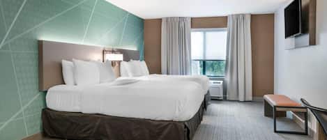 Una habitación de hotel con una cama grande, un banco, un televisor y un ventanal con cortinas.