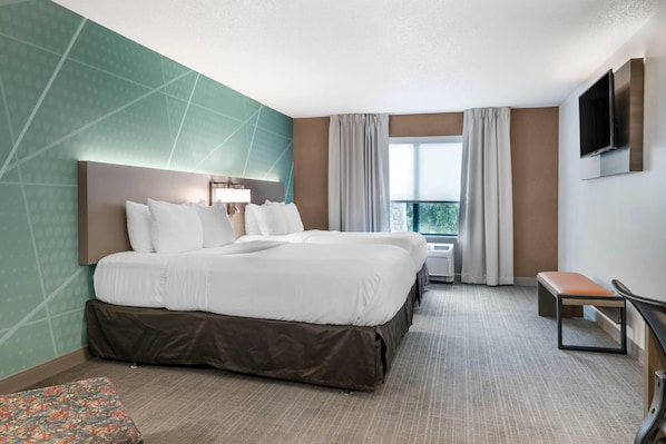 Una habitación de hotel con una cama grande, un banco, un televisor y un ventanal con cortinas.
