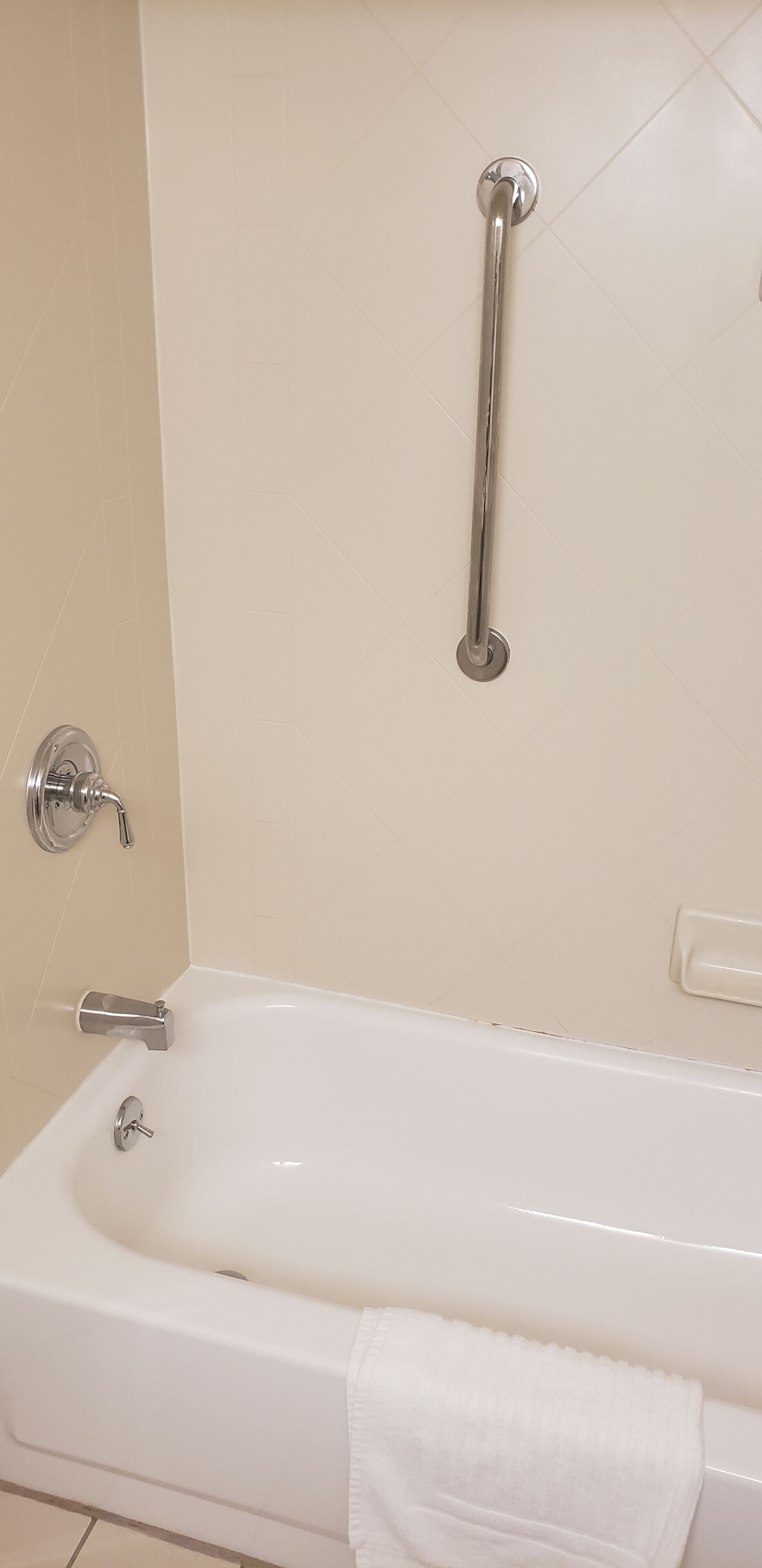 A white bathtub with a grab bar, a faucet, and a towel.