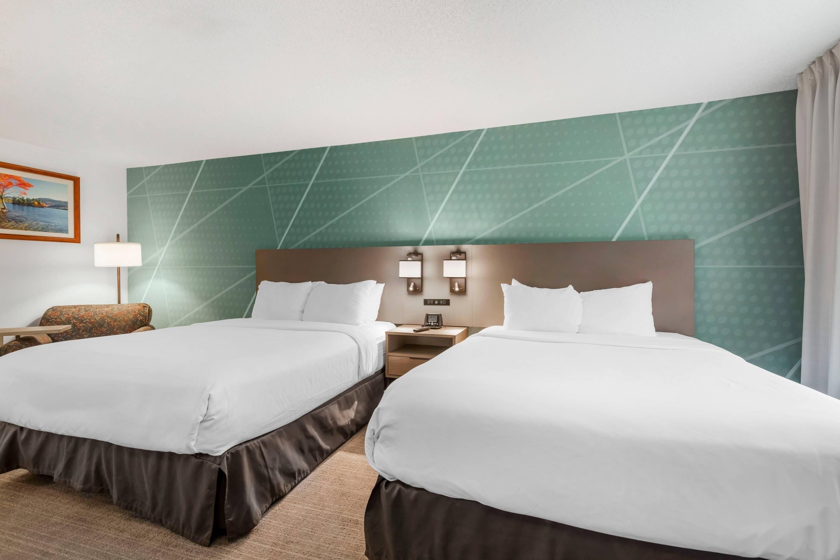 Habitación de hotel con dos camas, una mesita de noche, una lámpara y un cuadro en la pared.