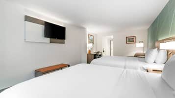 A hotel room with two beds, a desk, a chair, a TV, and a bathroom visible through an open door.