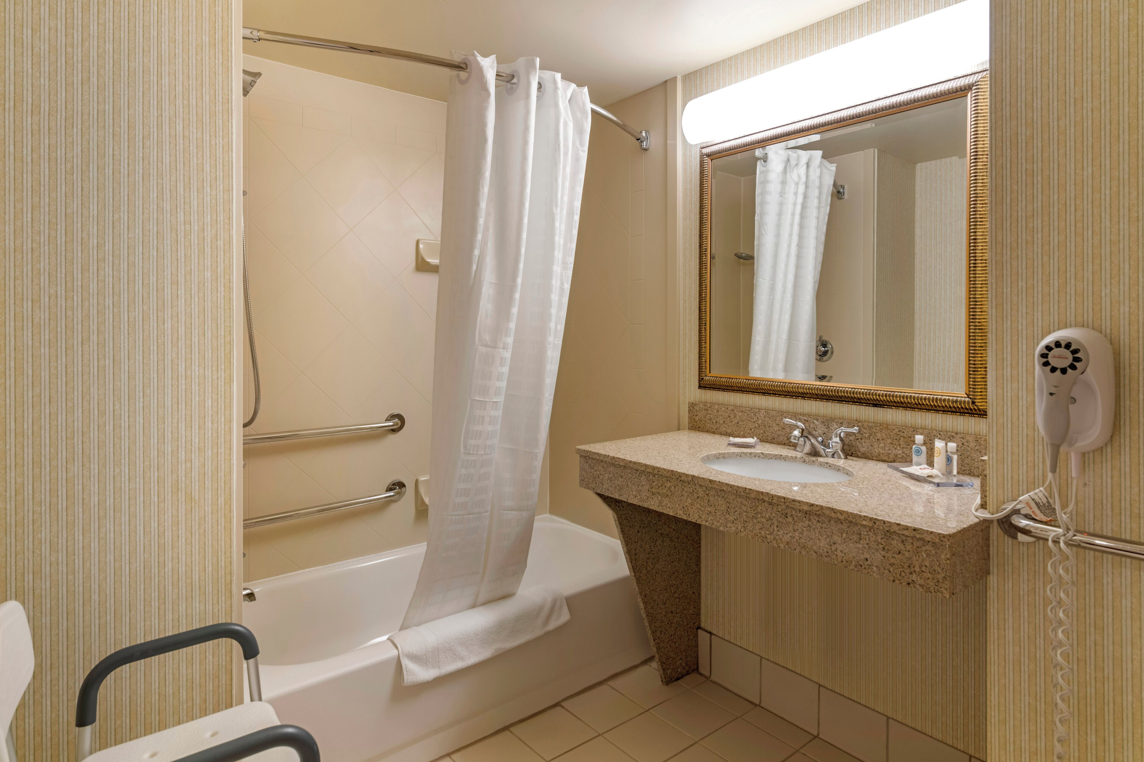 A bathroom with a bathtub, a shower curtain, a sink with a mirror, and a hairdryer.