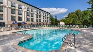 A hotel pool area with lounge chairs and umbrellas, a clear sky, and a building with multiple windows. - Comfort Inn & Suites Lake George (Lake George)