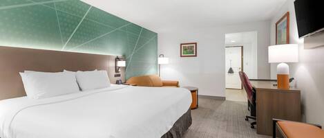 Habitación de hotel con una cama grande, un escritorio, una silla, un televisor y una lámpara.