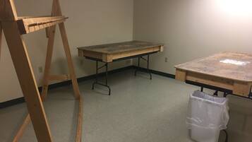 A room with a wooden easel, a large work table, and a trash bin.