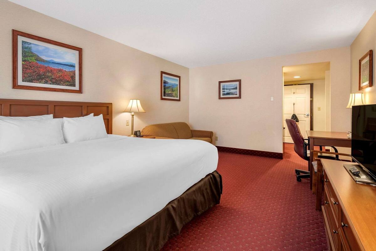 A hotel room with a large bed, a desk with a chair, a TV, and two framed pictures on the wall.