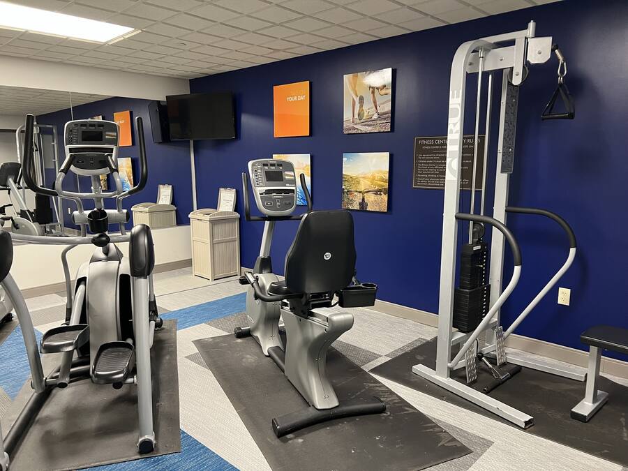 Un gimnasio con máquinas de cardio, una banca de pesas y una televisión instalada en la pared.