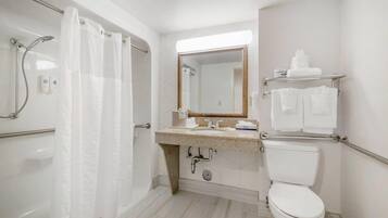 Baño con ducha, inodoro, lavamanos y espejo.