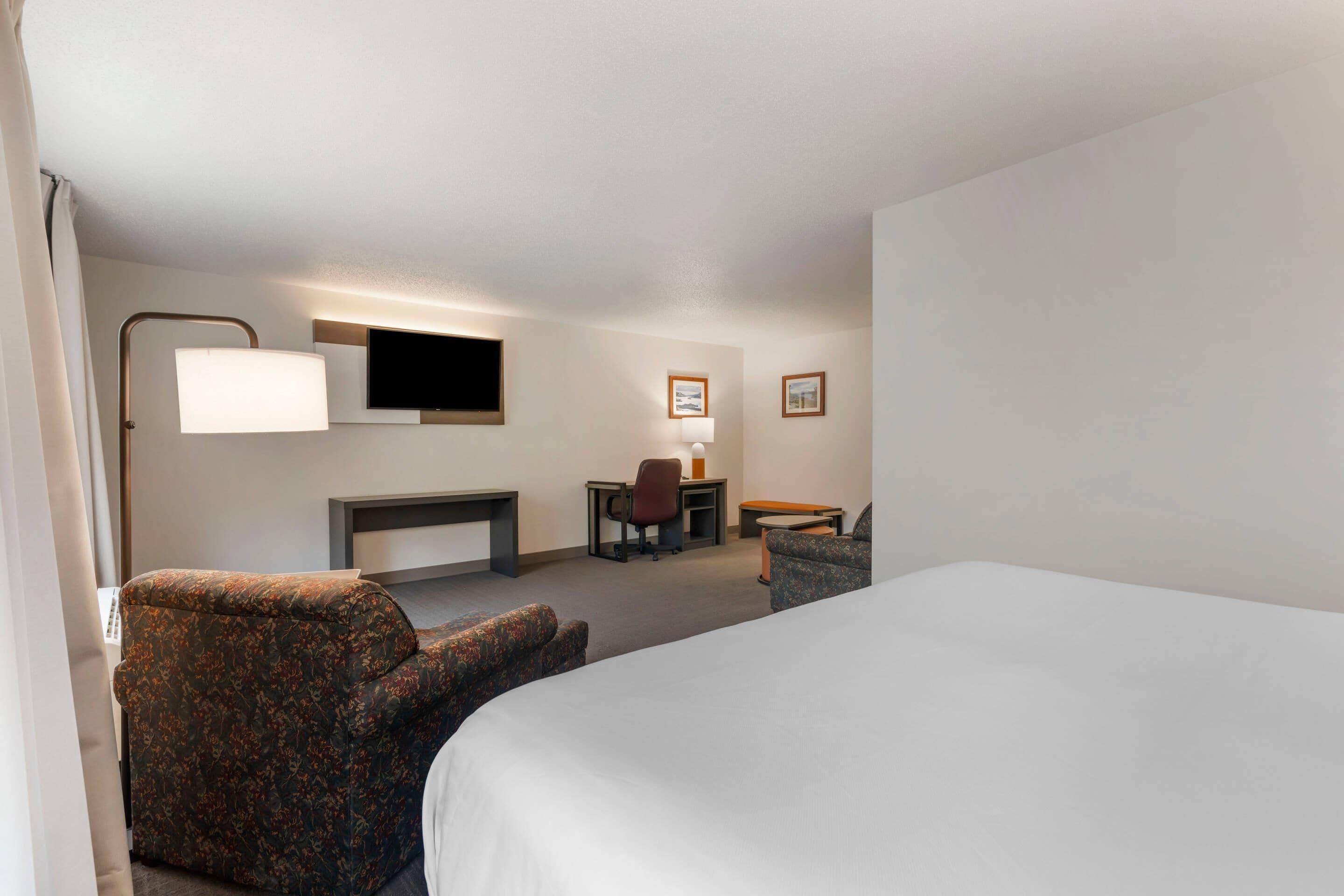 A hotel room with a bed, a desk, a chair, a TV, and a lamp.