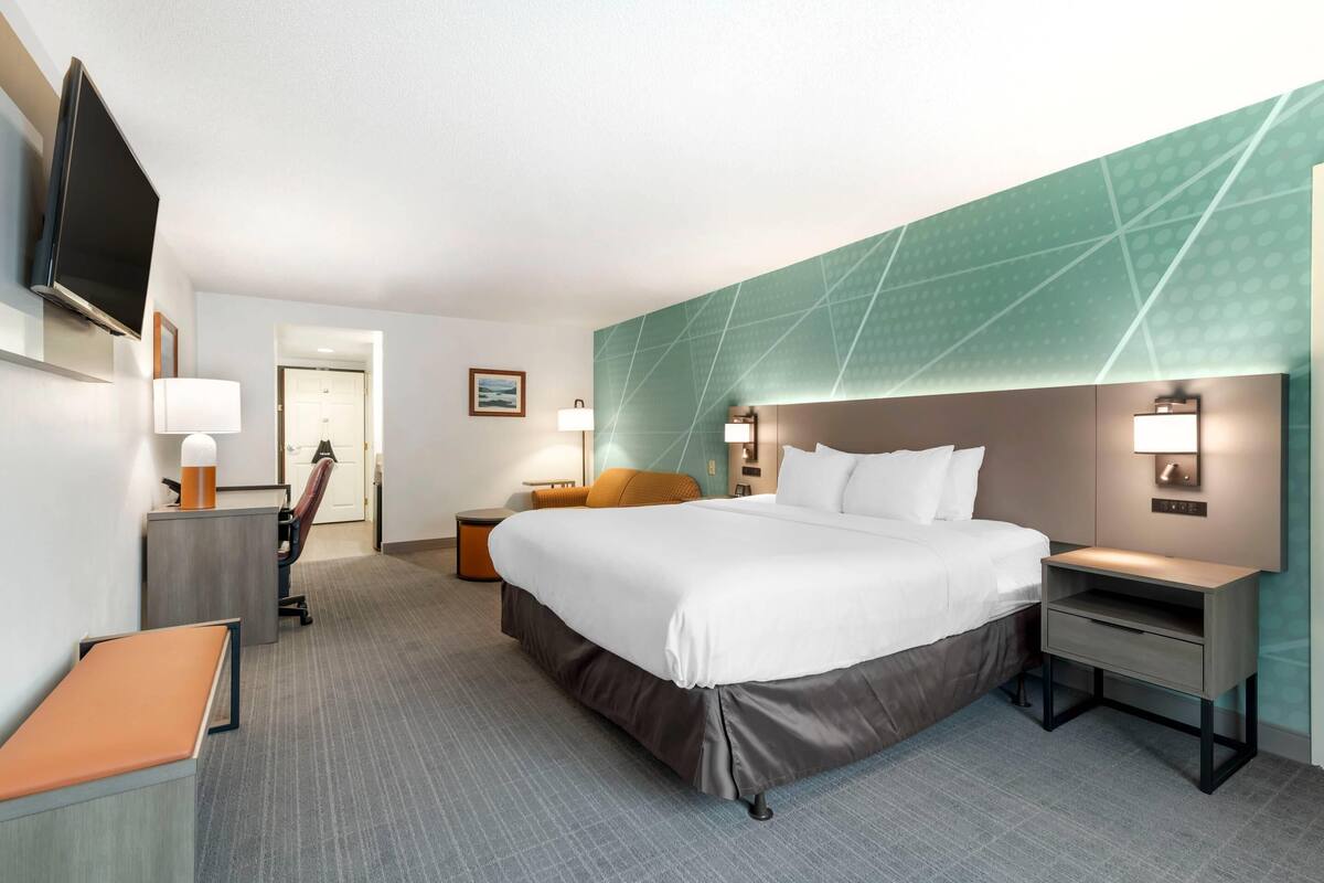 A hotel room with a bed, bedside tables, a desk, a chair, a TV, and a door.