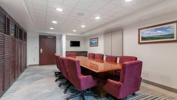 A conference room with a large table, red chairs, a TV, and framed pictures on the walls.