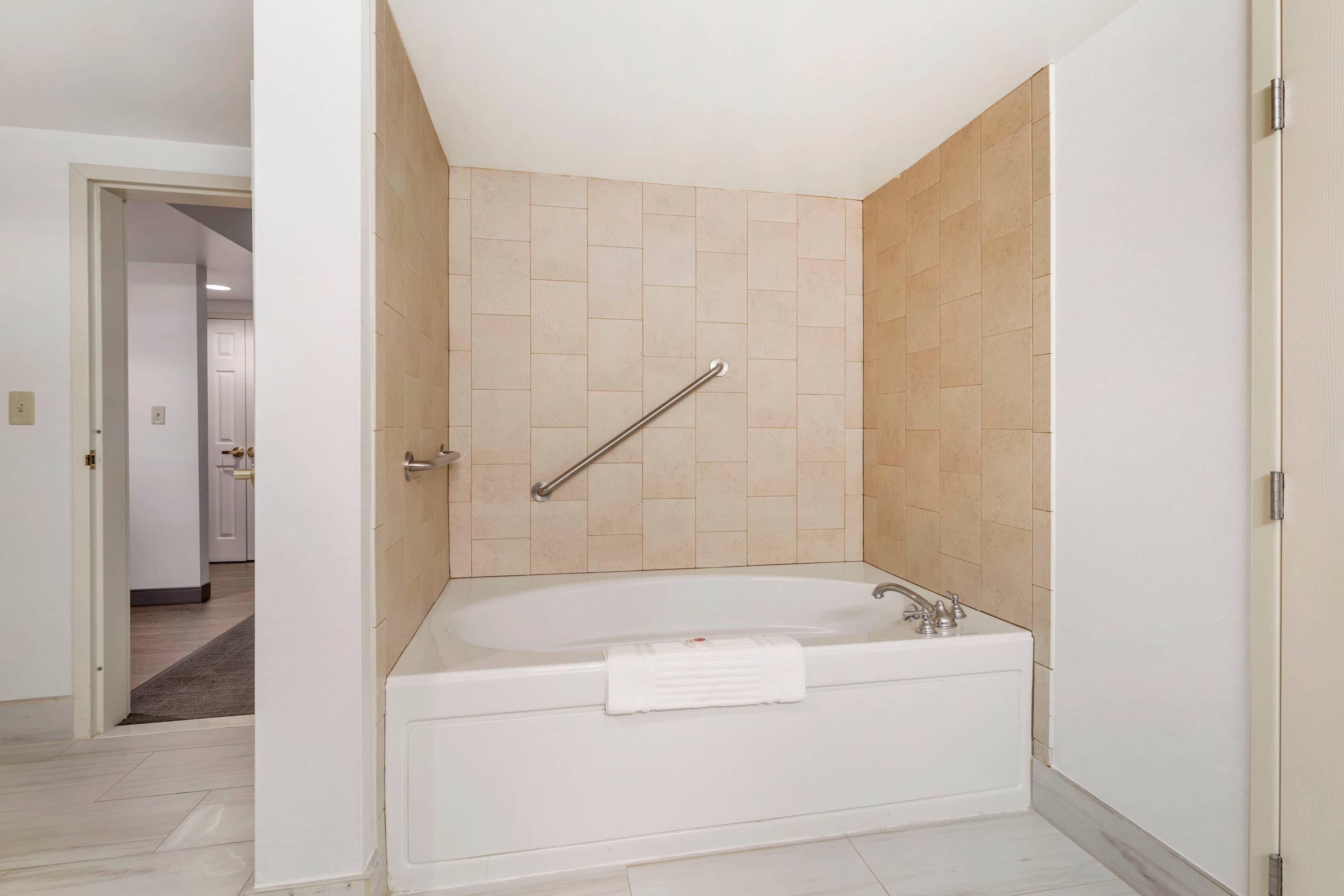 A modern bathroom with a bathtub, a shower area with a handrail, and a visible door leading to another room.
