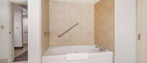 A modern bathroom with a bathtub, a shower area with a handrail, and a visible door leading to another room.